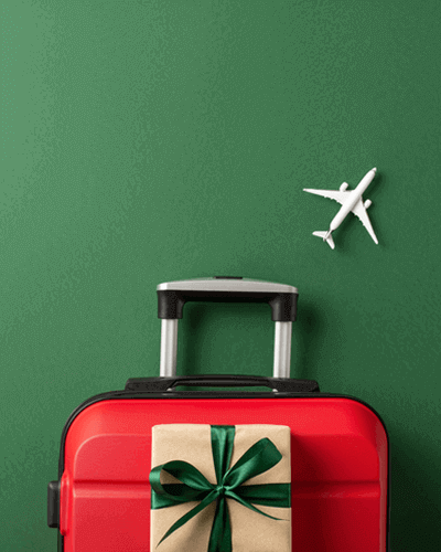 Shot of a suitcase, miniature airplane model, and craft paper giftbox on green background